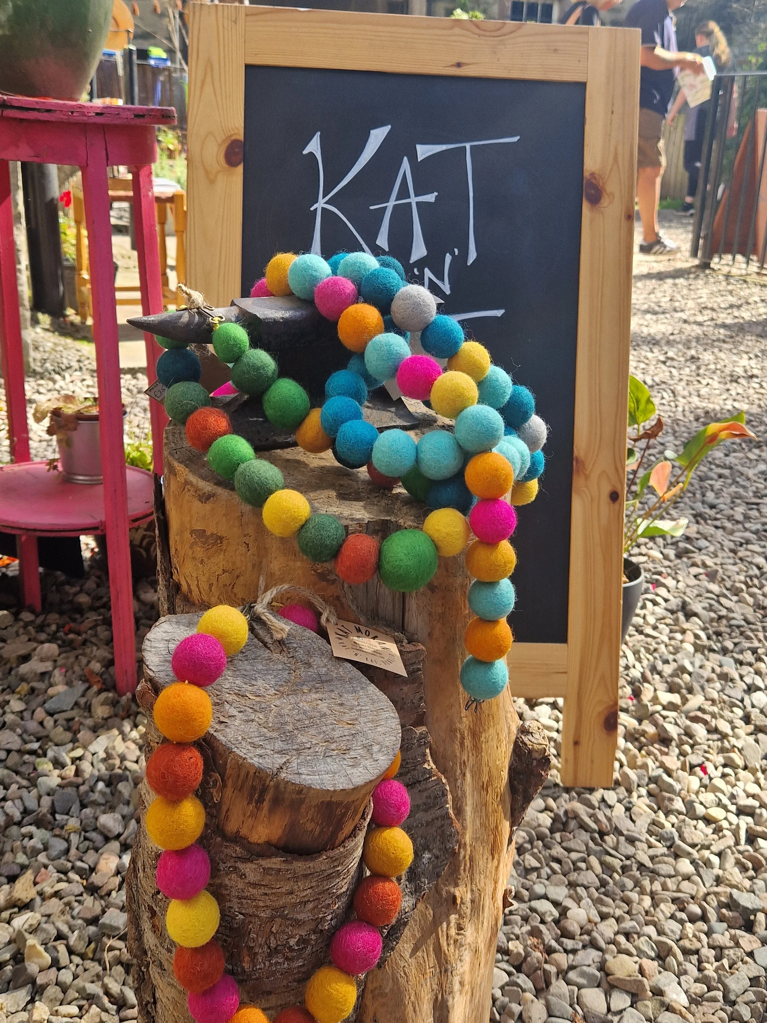 Colorful felted wool bead necklaces displayed on a wooden stand outside at a market or shop.