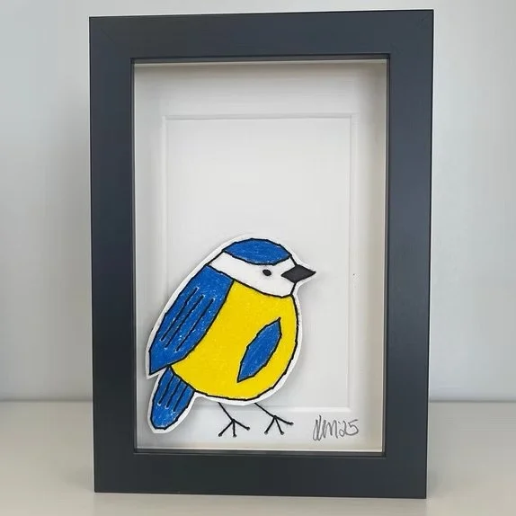 Framed embroidered artwork of a blue and yellow bird on a white background.