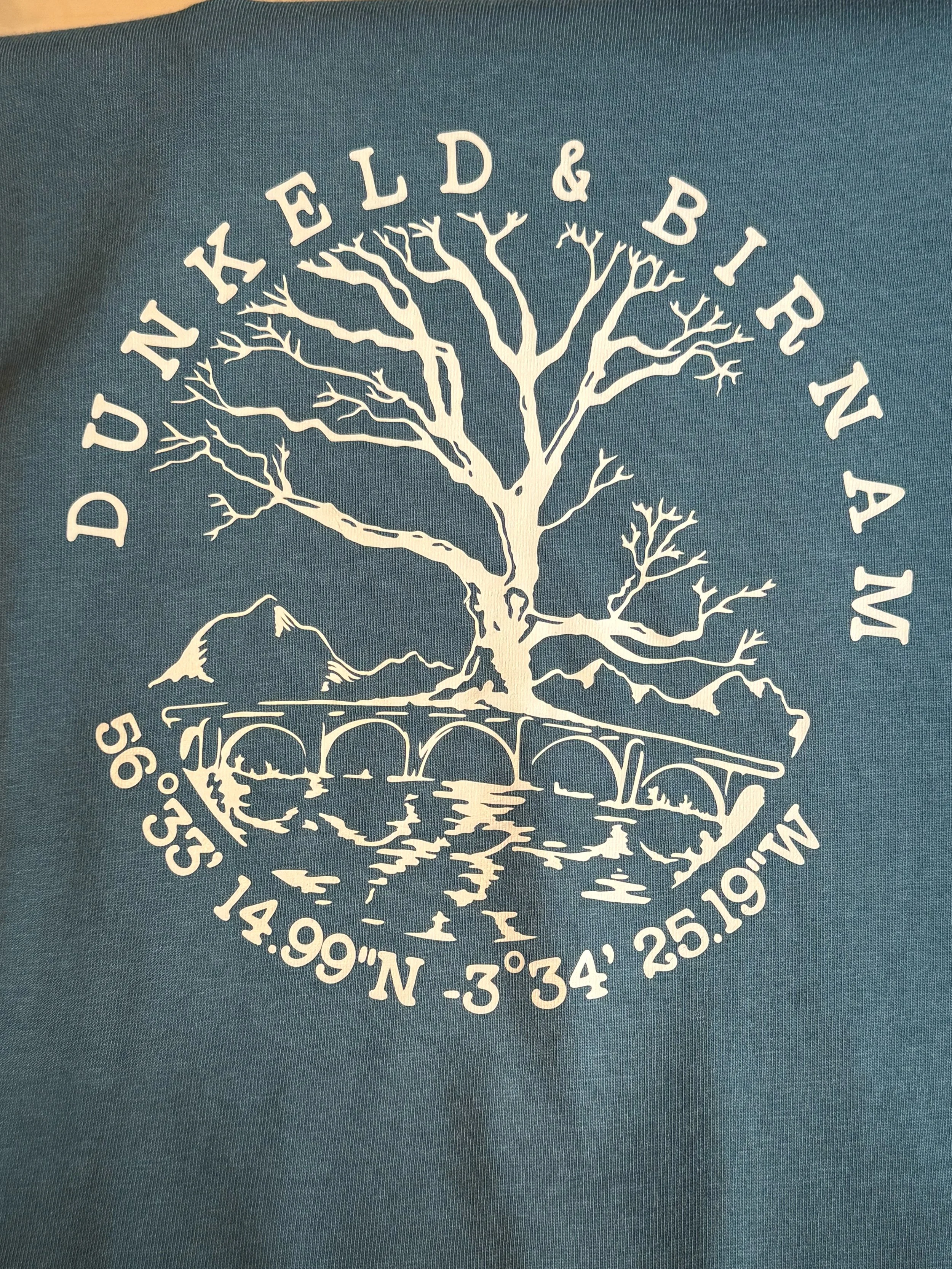 A graphic design featuring a large leafless tree above a bridge, with surrounding mountain and water reflections. Text encircles the design, including 'DUI KELED & BIR NAM', geographic coordinates '56°53'14.99"N -3°34'25.19"E', and other words.
