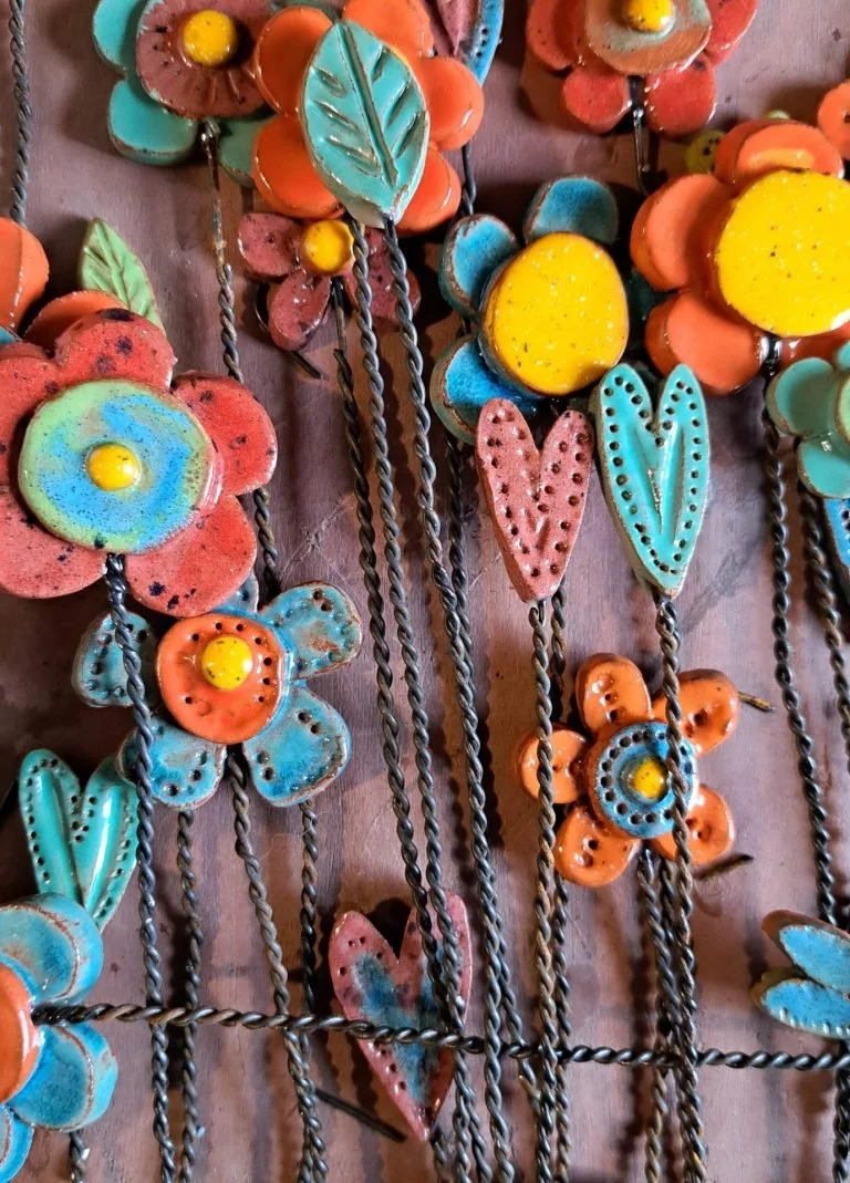 Colorful metal flower and heart-shaped decorations with intricate designs, arranged on a wire grid.