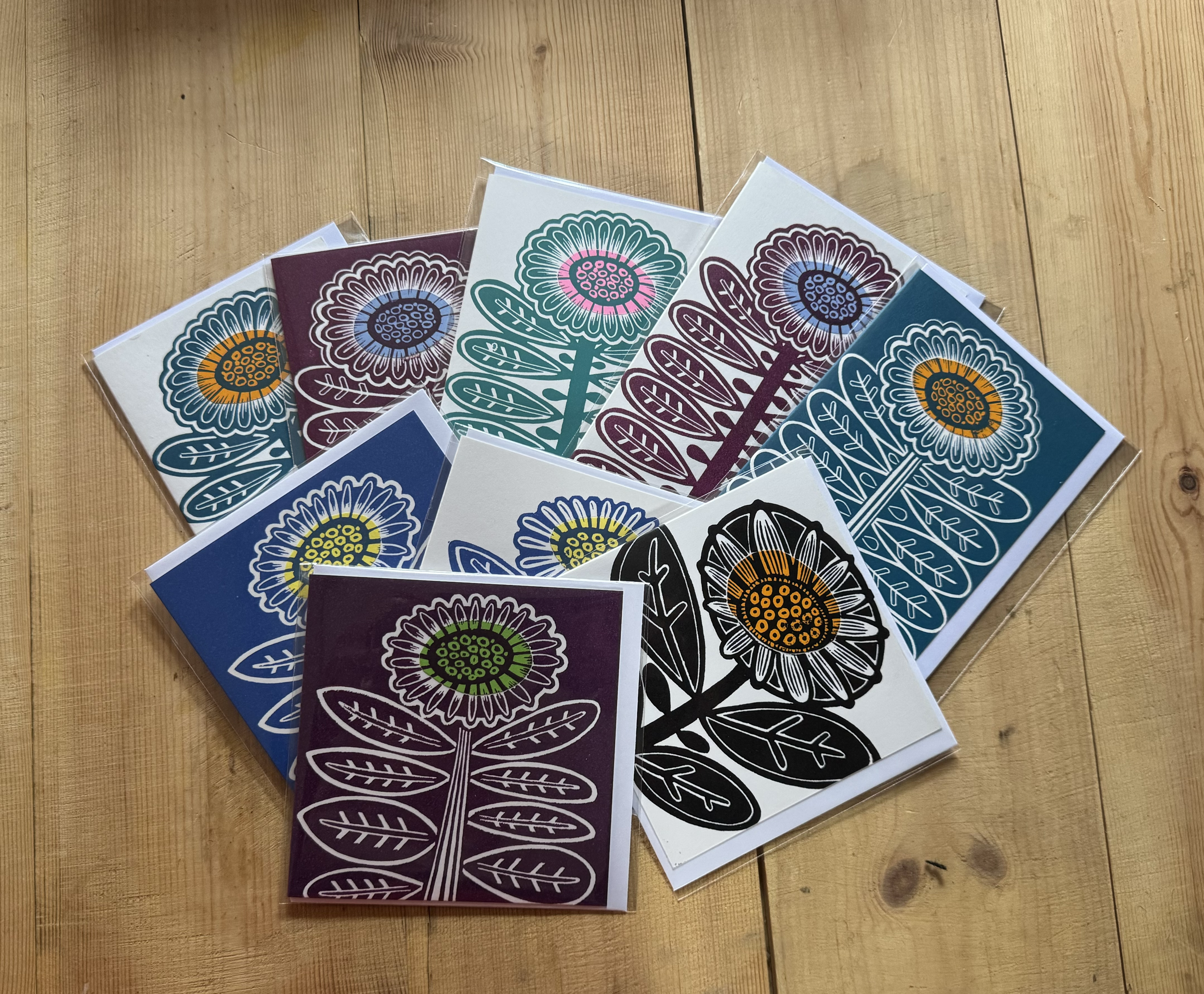 Multiple colorful floral art prints featuring stylized flowers and leaves, wrapped in plastic, spread on a wooden surface.