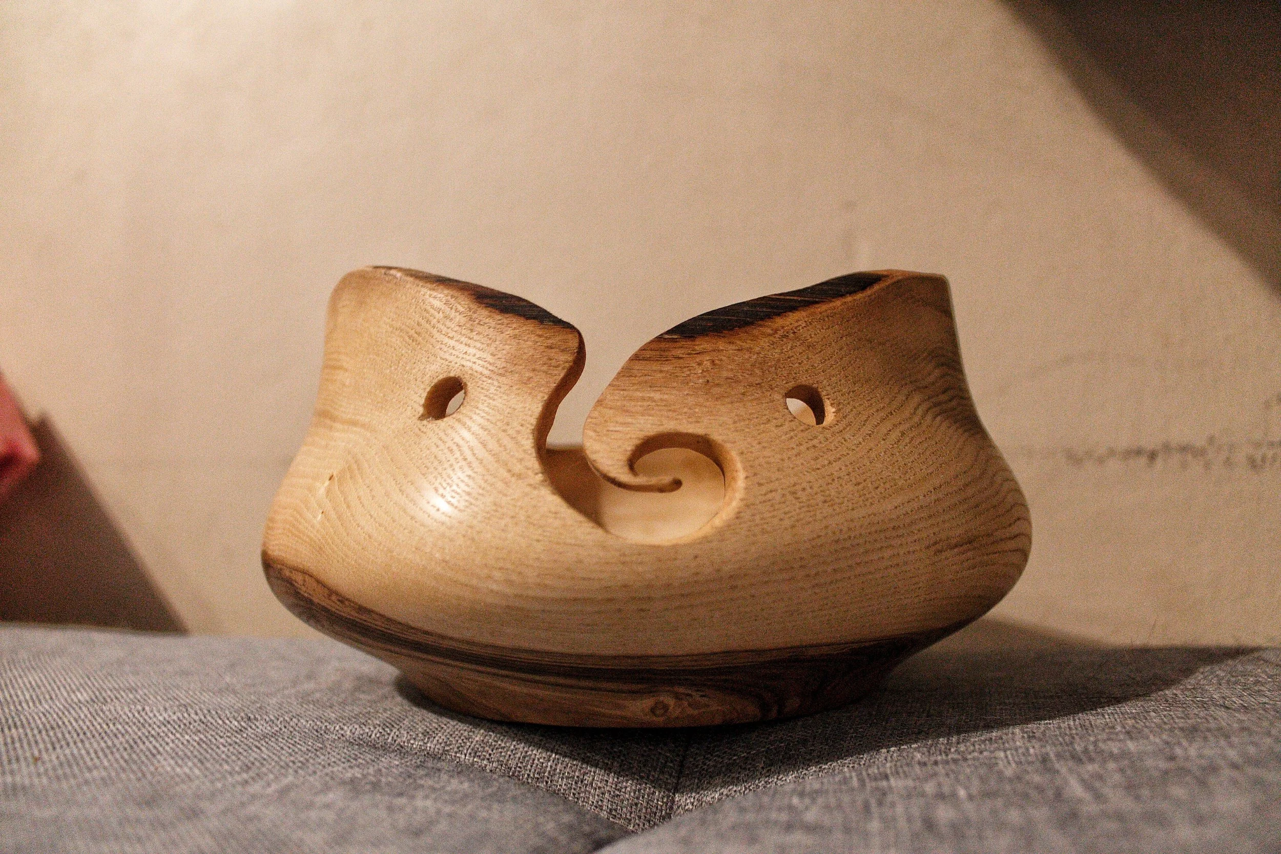 Wooden yarn bowl with decorative holes and spiral opening on fabric surface.