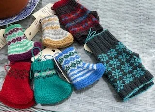Multiple colorful knitted baby socks and mittens displayed on a light surface.