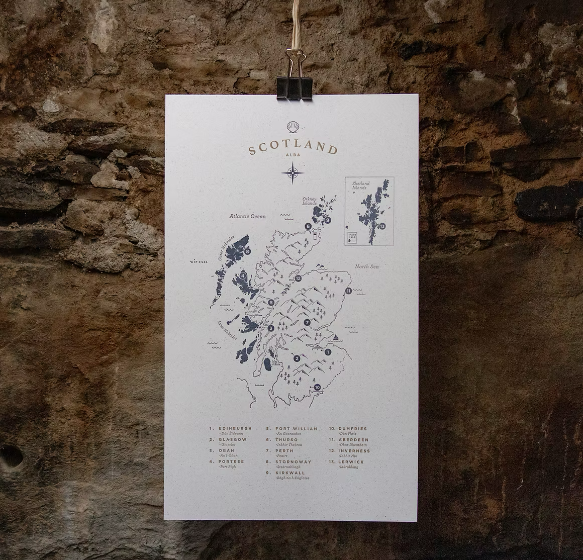 A map of Scotland hanging on a stone wall, listing major cities and regions.