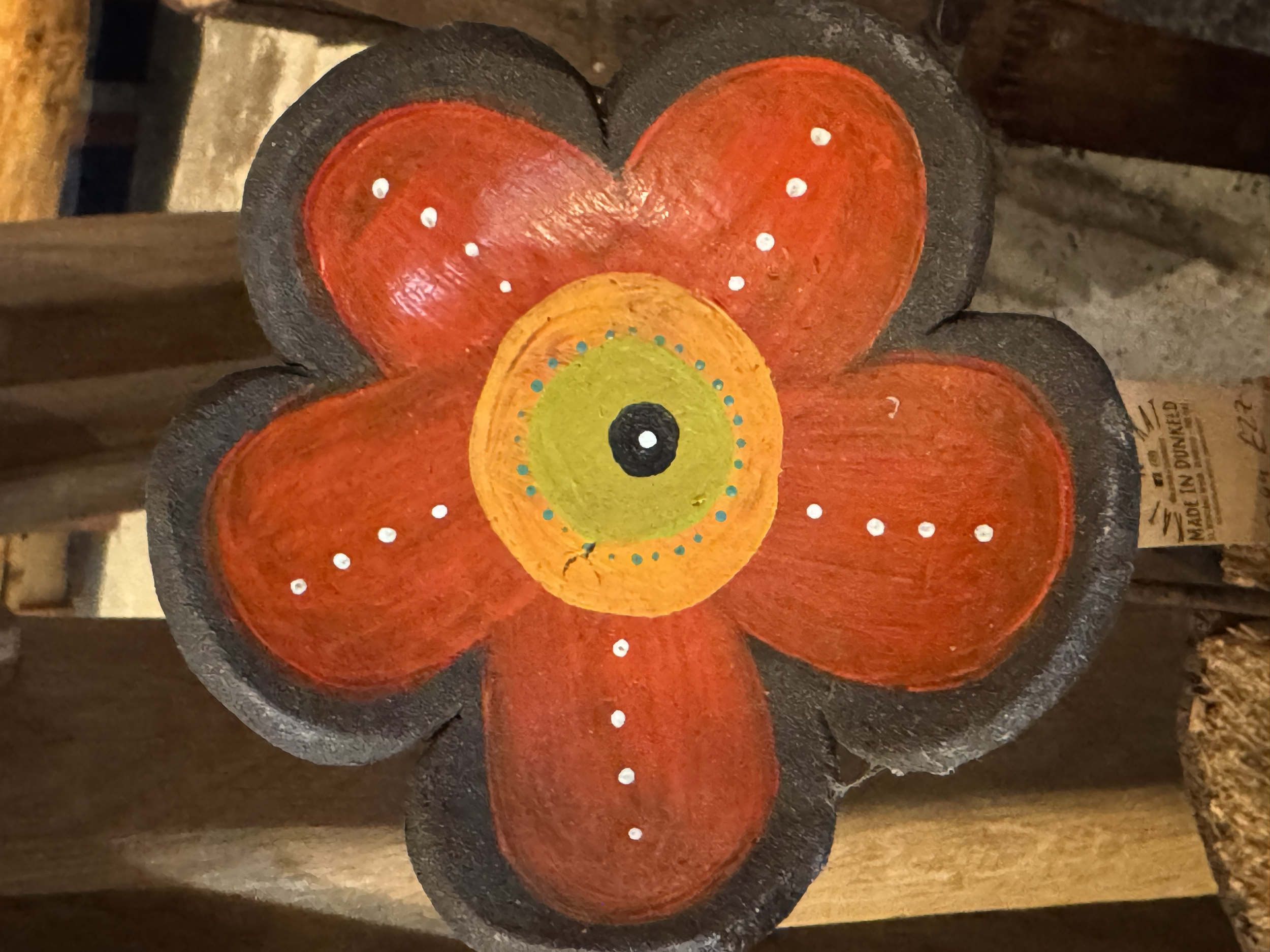 Decorative flower-shaped candle with orange, green, black, and white colors, resting on a wooden surface.