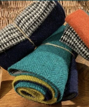 Rolled and folded patterned and solid color fabrics on a wooden surface.