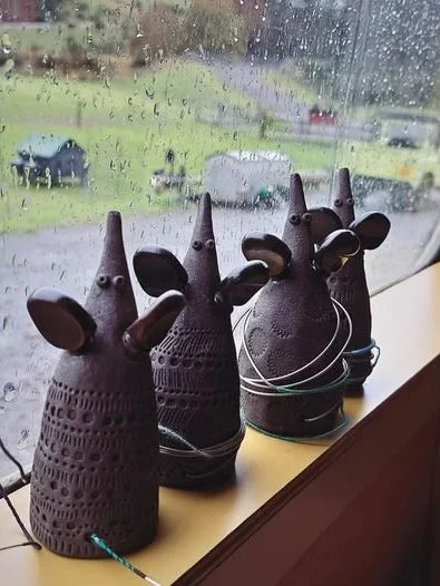 Three decorative rabbit-shaped ceramic figurines with open ears, sitting on a window ledge with rain-drenched outdoors visible through the window.