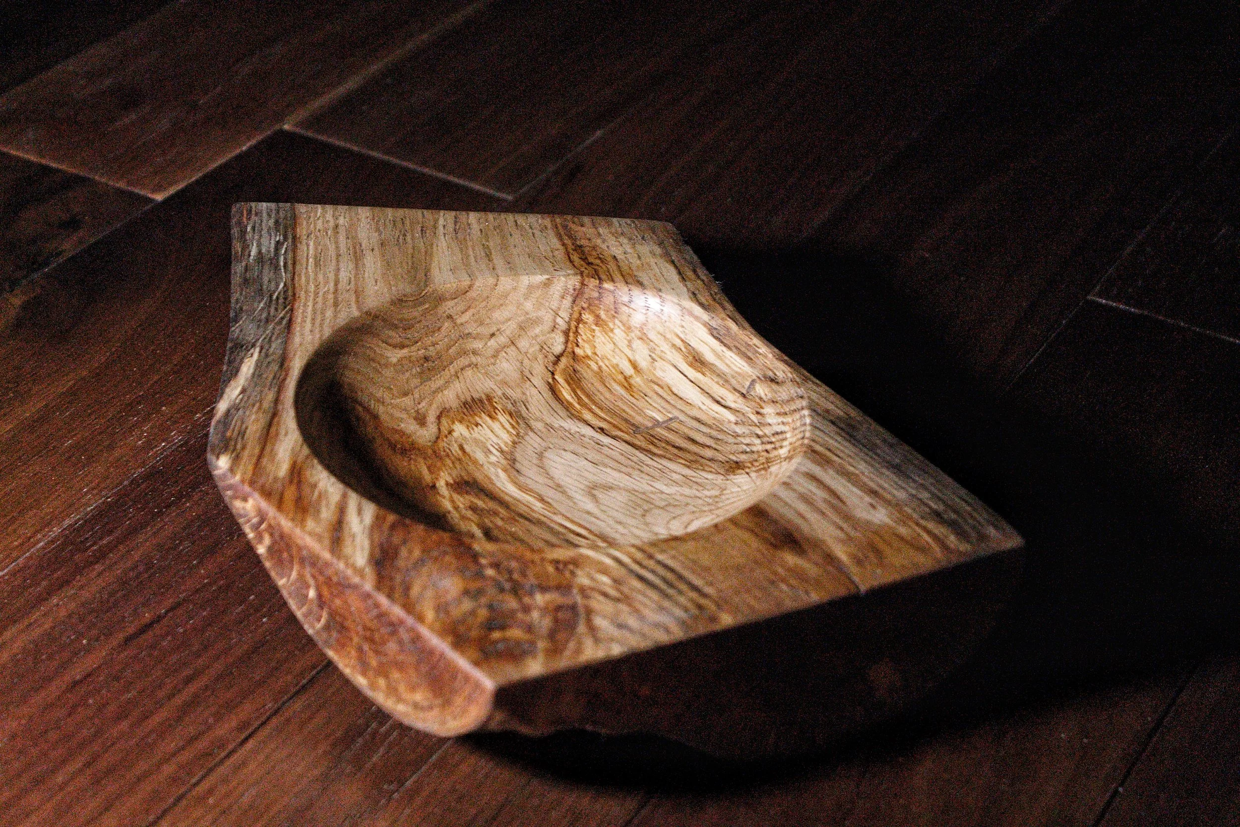 Close-up of a handcrafted wooden bowl on a wooden surface, showcasing natural wood grain and irregular shape.