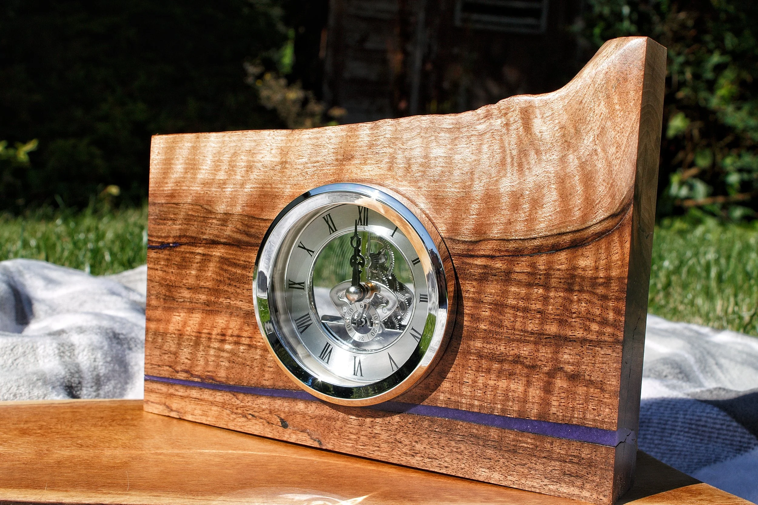 Wooden clock with a visible mechanical movement and Roman numerals on a grassy background.