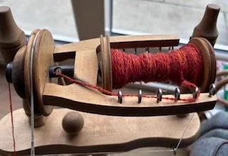 A wooden spinning wheel with red yarn wound around its spindle.