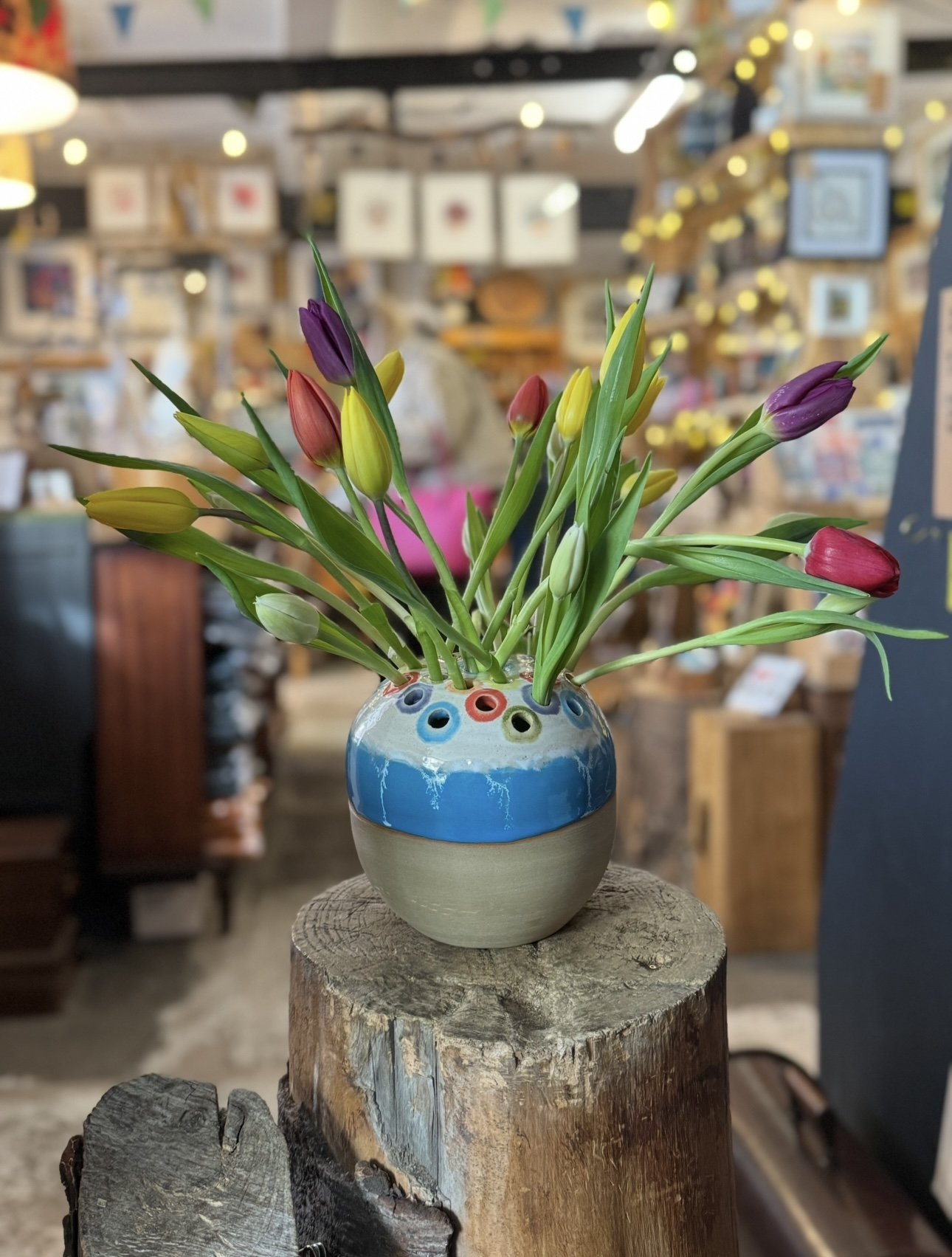 Colorful ceramic vase filled with multicolored tulips on a wooden surface in a store setting.