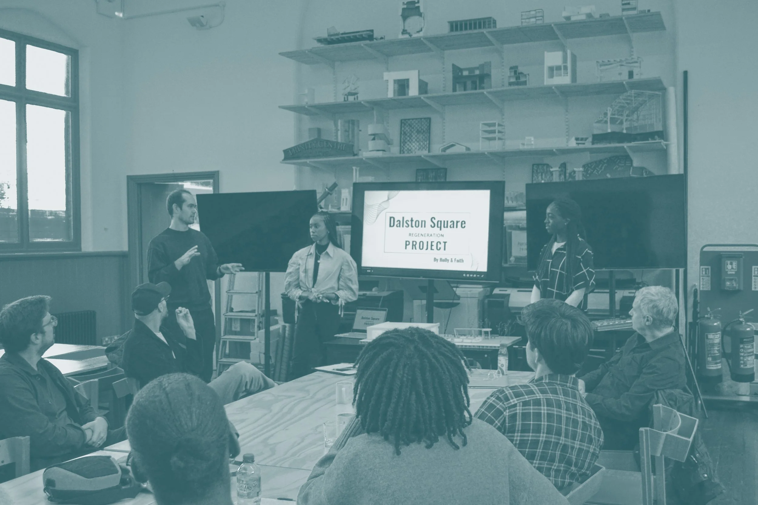 People attending a presentation about a regeneration project at Dalston Square, with three individuals standing in front of a presentation screen.