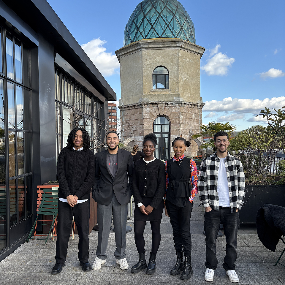 Group of five people smiling and standing together on a rooftop terrace with a historic building featuring a glass dome in the background.