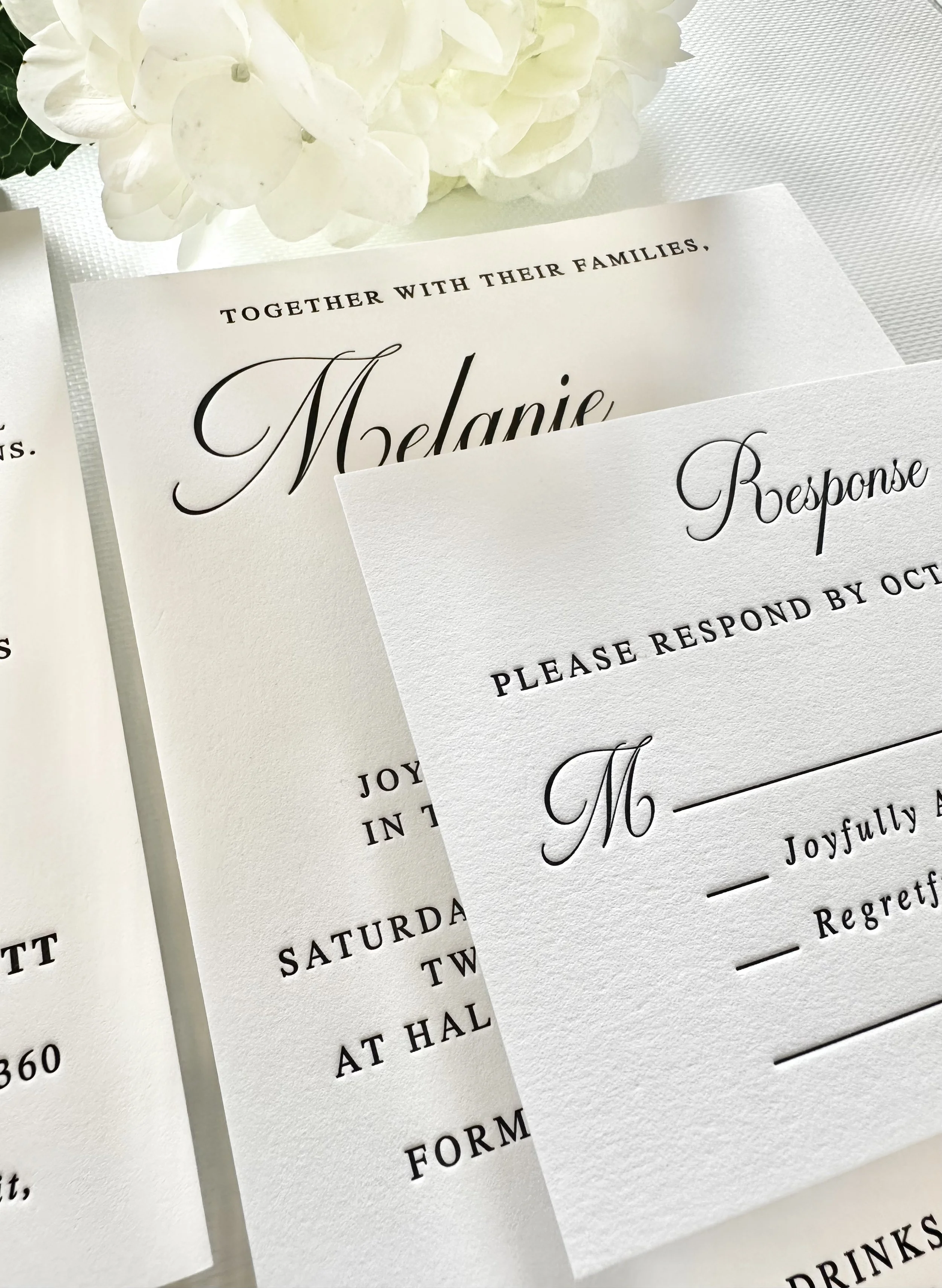 Wedding invitation and RSVP card with elegant typography next to white flowers.