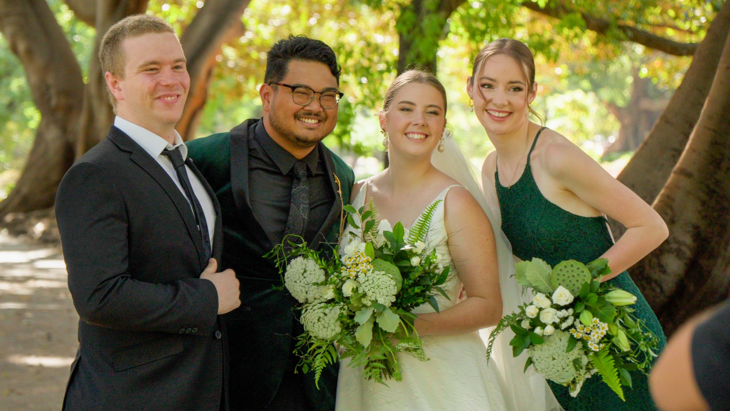 Four people at a wedding, with the bride holding a bouquet, standing in a garden.