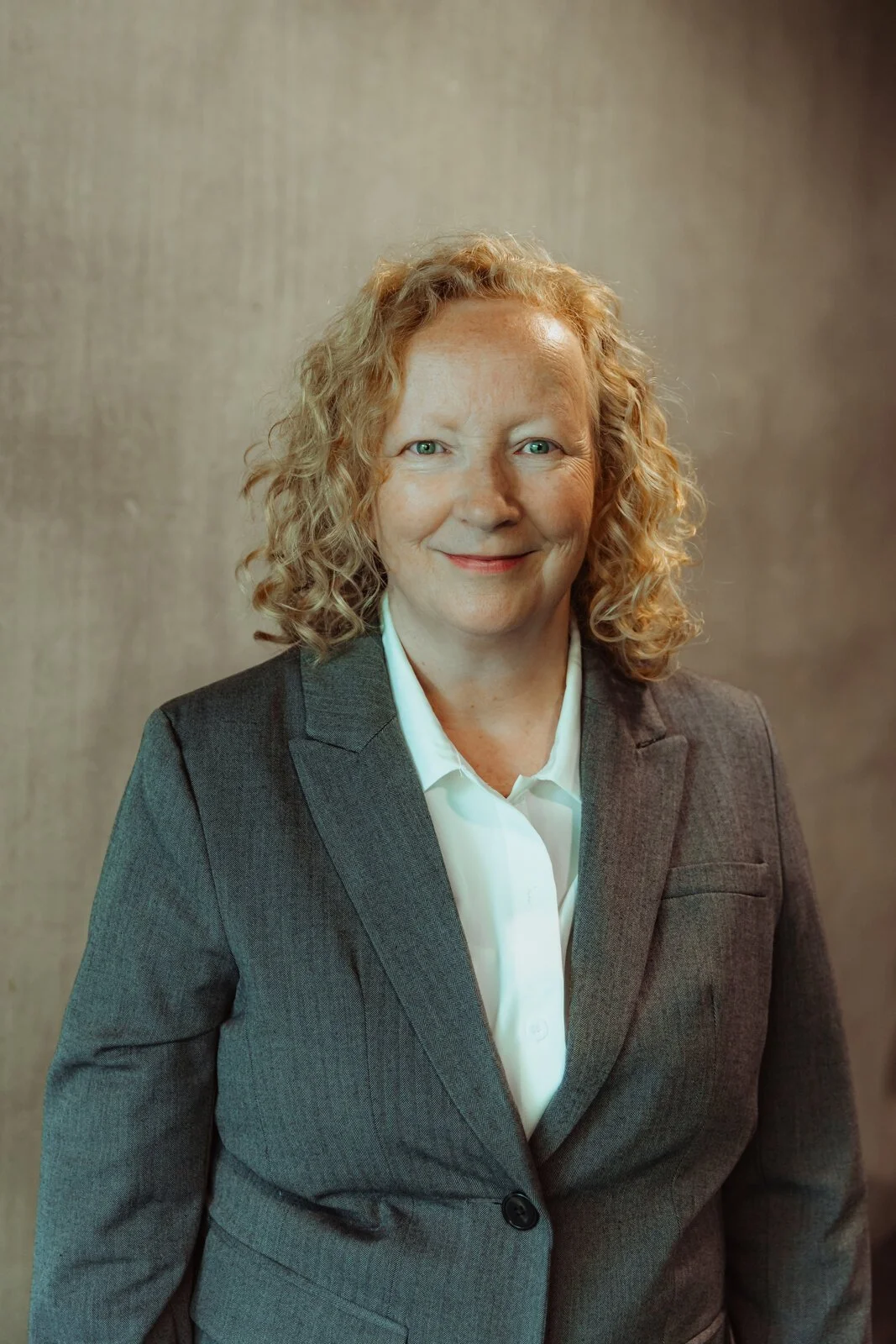 Saskia, Betwixt dancer, smiling in a grey herringbone blazer with curly strawberry-blonde hair.