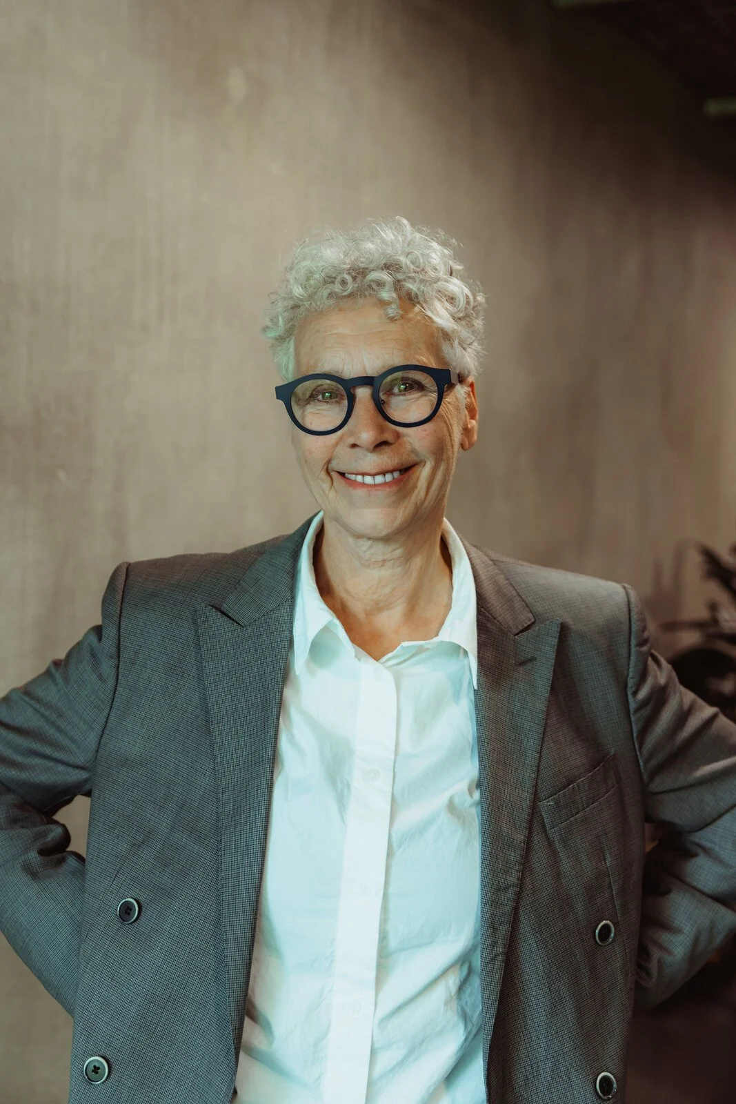 Gill, Betwixt dancer, laughing in a grey blazer with short white curly hair and dark glasses.