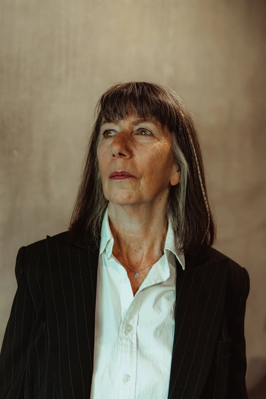 Helen Tate, Betwixt dancer, looking upward in a black pinstripe blazer with a fringed hairstyle and pendant necklace.