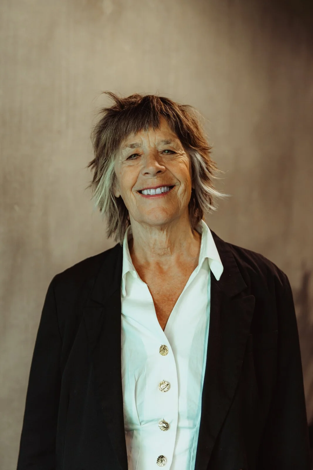 Maya, Betwixt dancer, smiling broadly in a black blazer with a choppy shag haircut.
