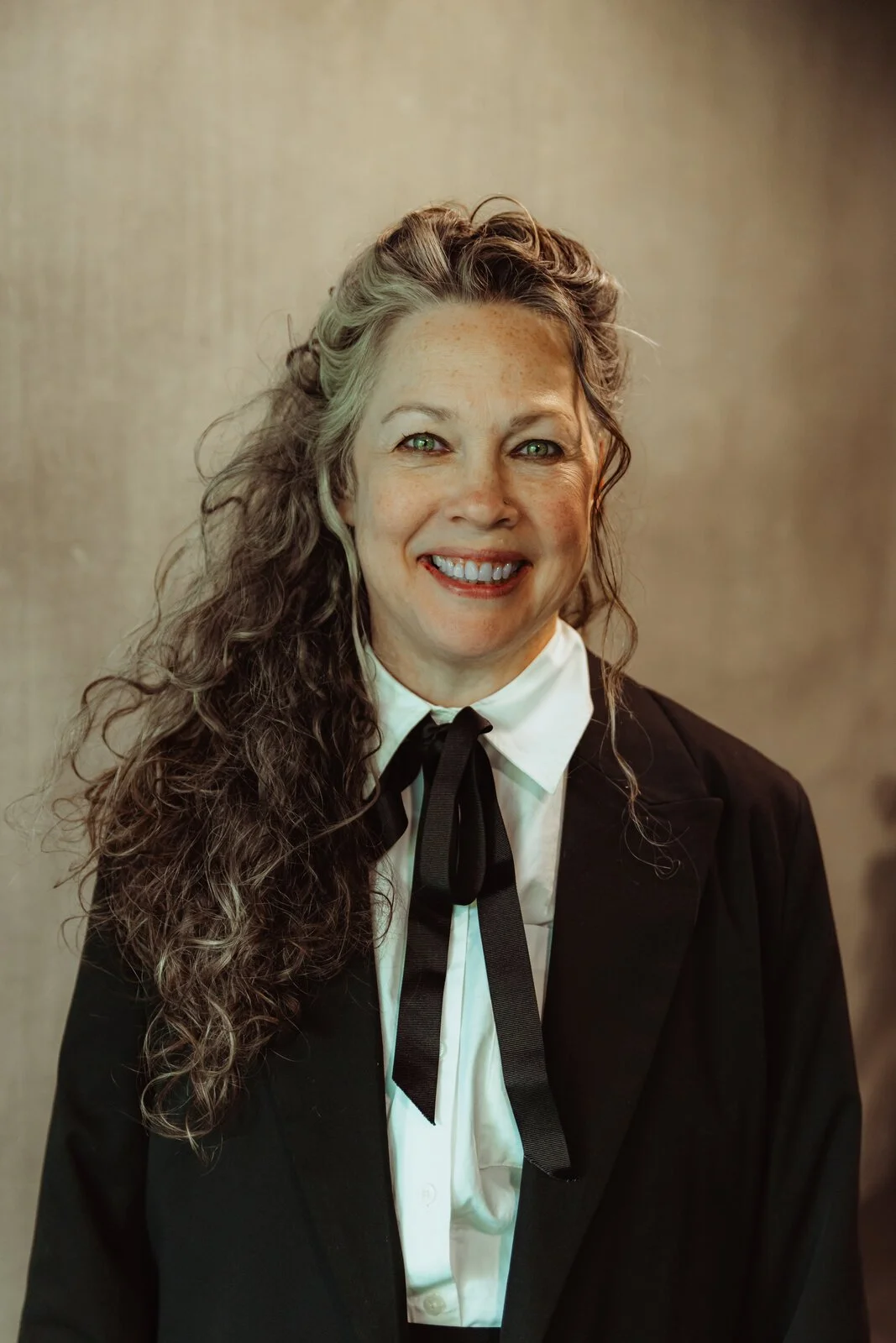 Helen Nelder, Betwixt dancer, smiling in a black blazer with a bow tie and long wavy grey-brown hair.