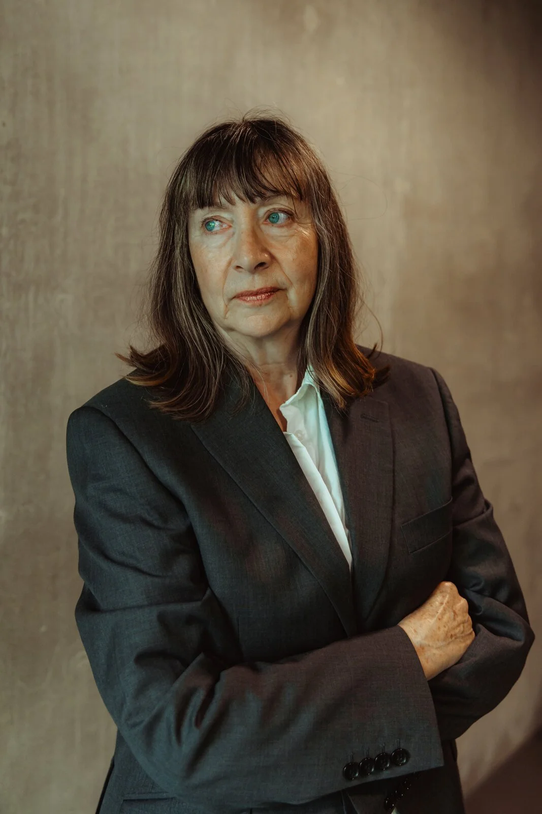Kate, Betwixt dancer, looking thoughtfully to the side in a grey blazer with arms crossed,