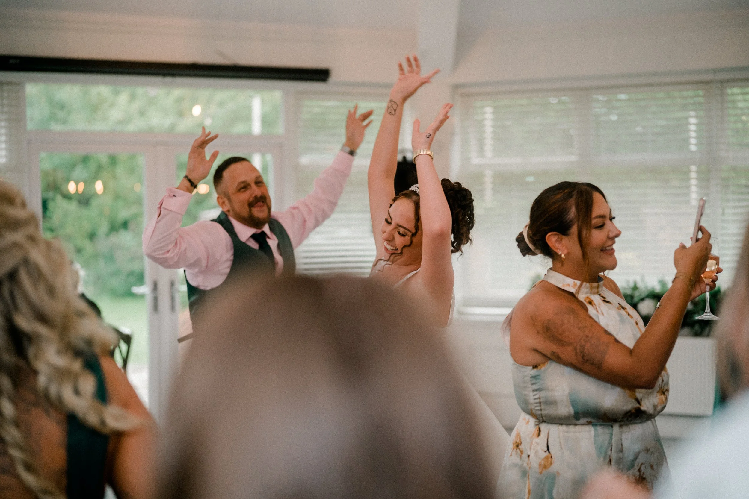 People dancing and celebrating indoors at a social gathering, with a woman smiling and looking at her phone.