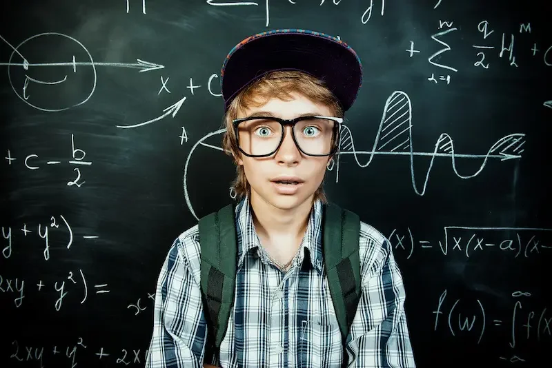 kid with big glasses against a chalkboard with writing on it