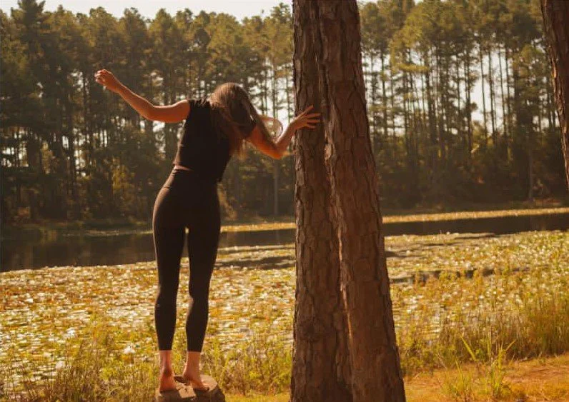 girl in black top and pants leaning on a tree