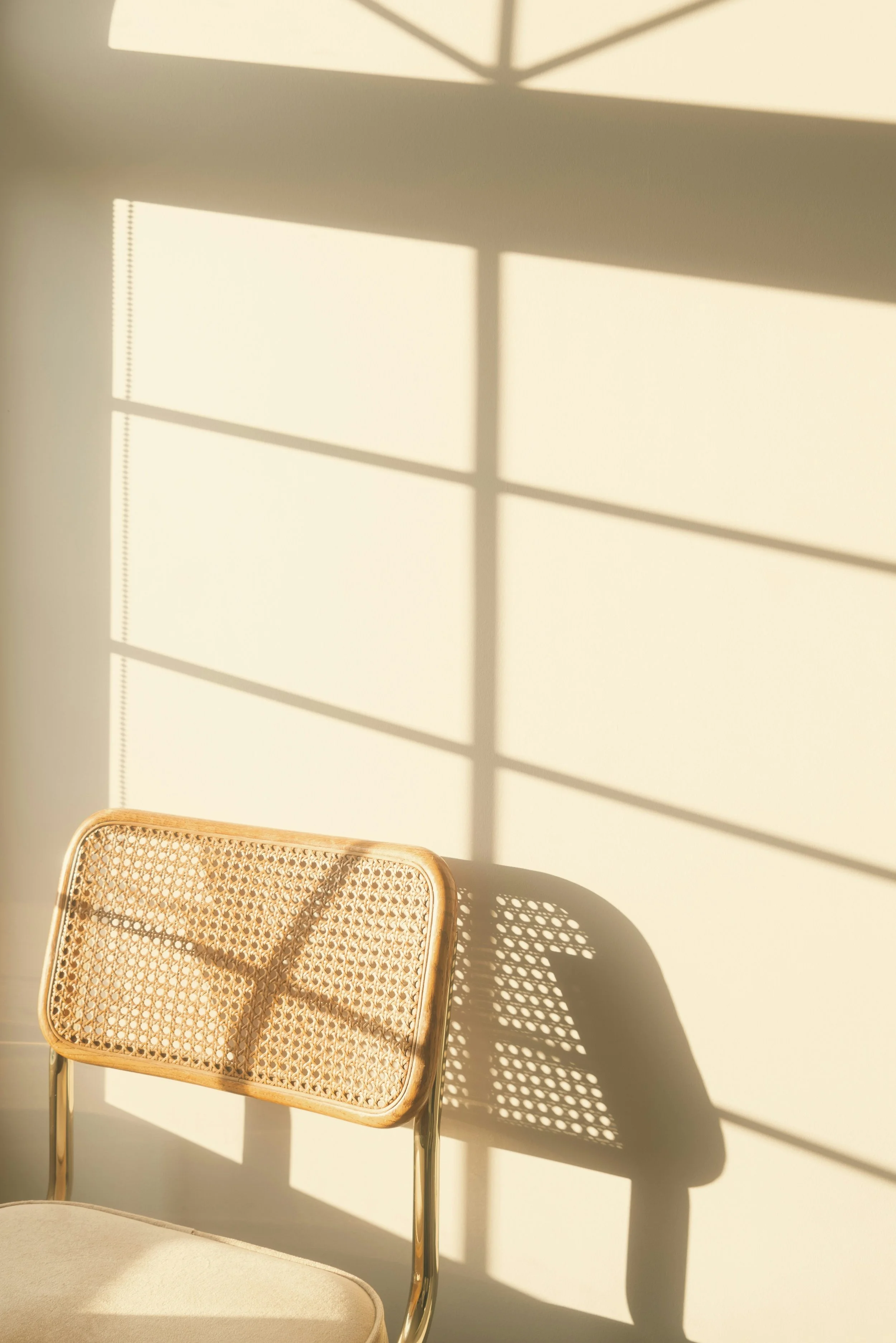 Cane chair with window light and shadow pattern on wall, evoking stillness and reflection.