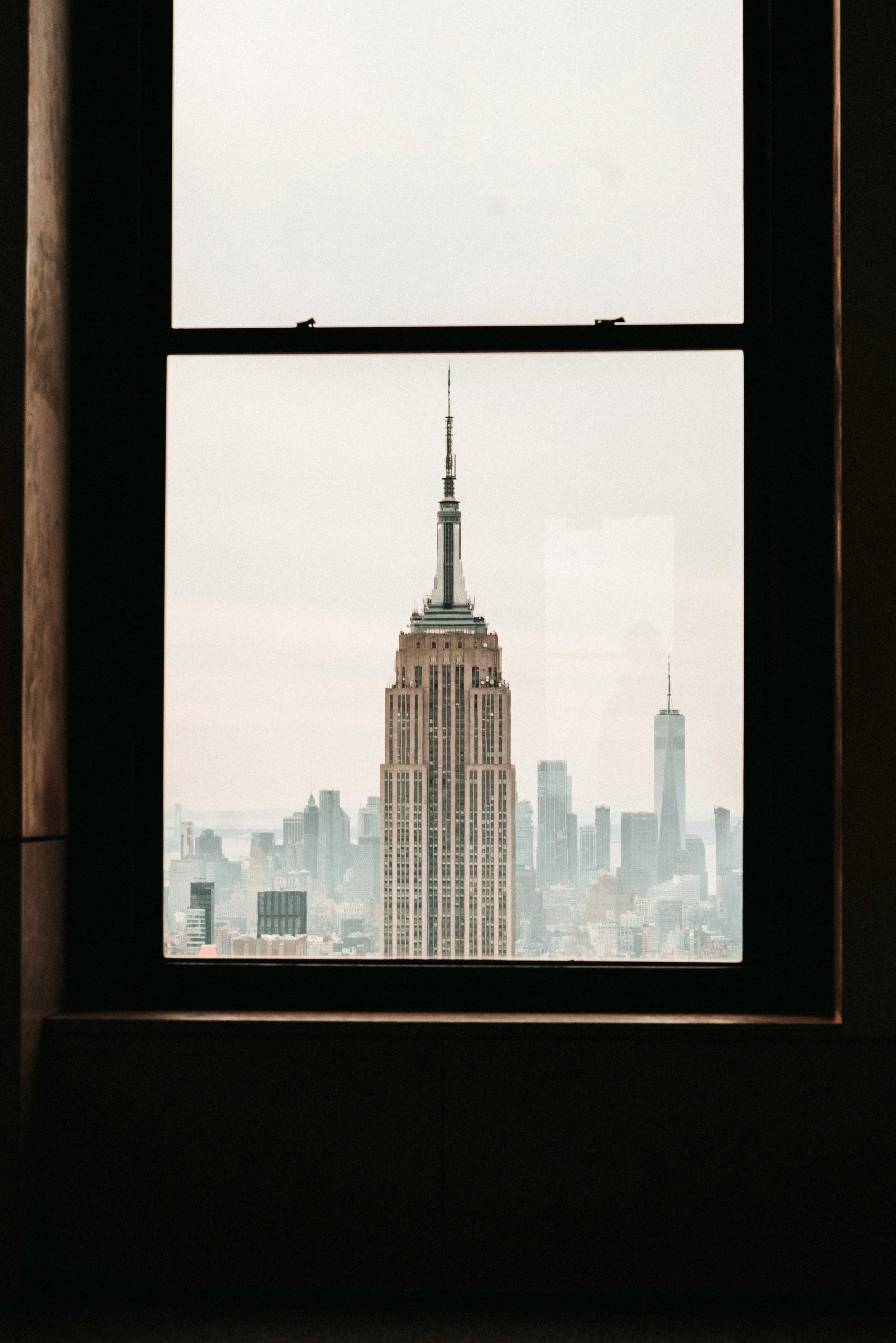 View of the New York City skyline through a window, including the Empire State Building.
