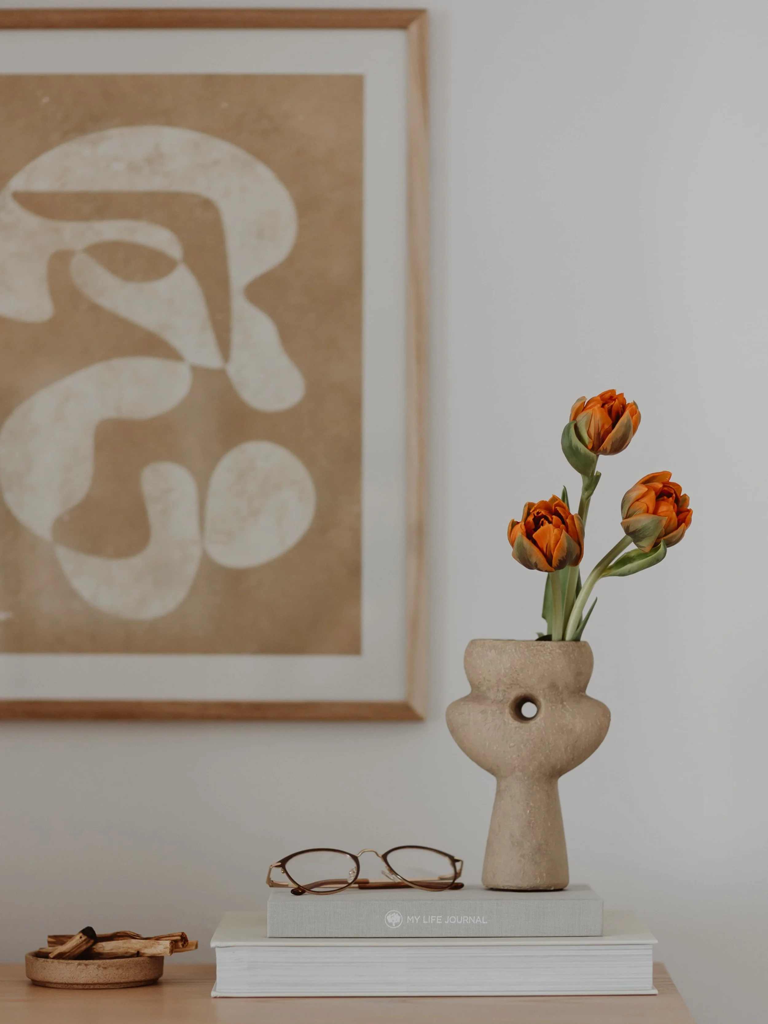 Minimal still life with books, glasses, and flowers in a softly lit apartment.