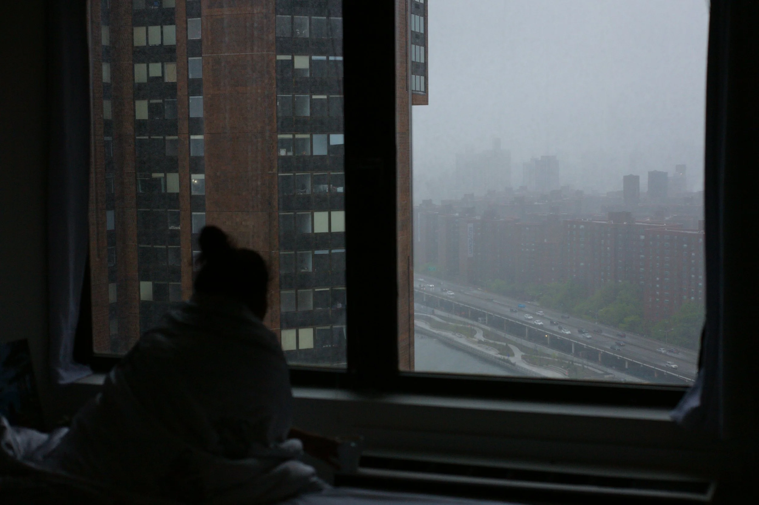 Person looking thoughtfully out the window on a grey, rainy day