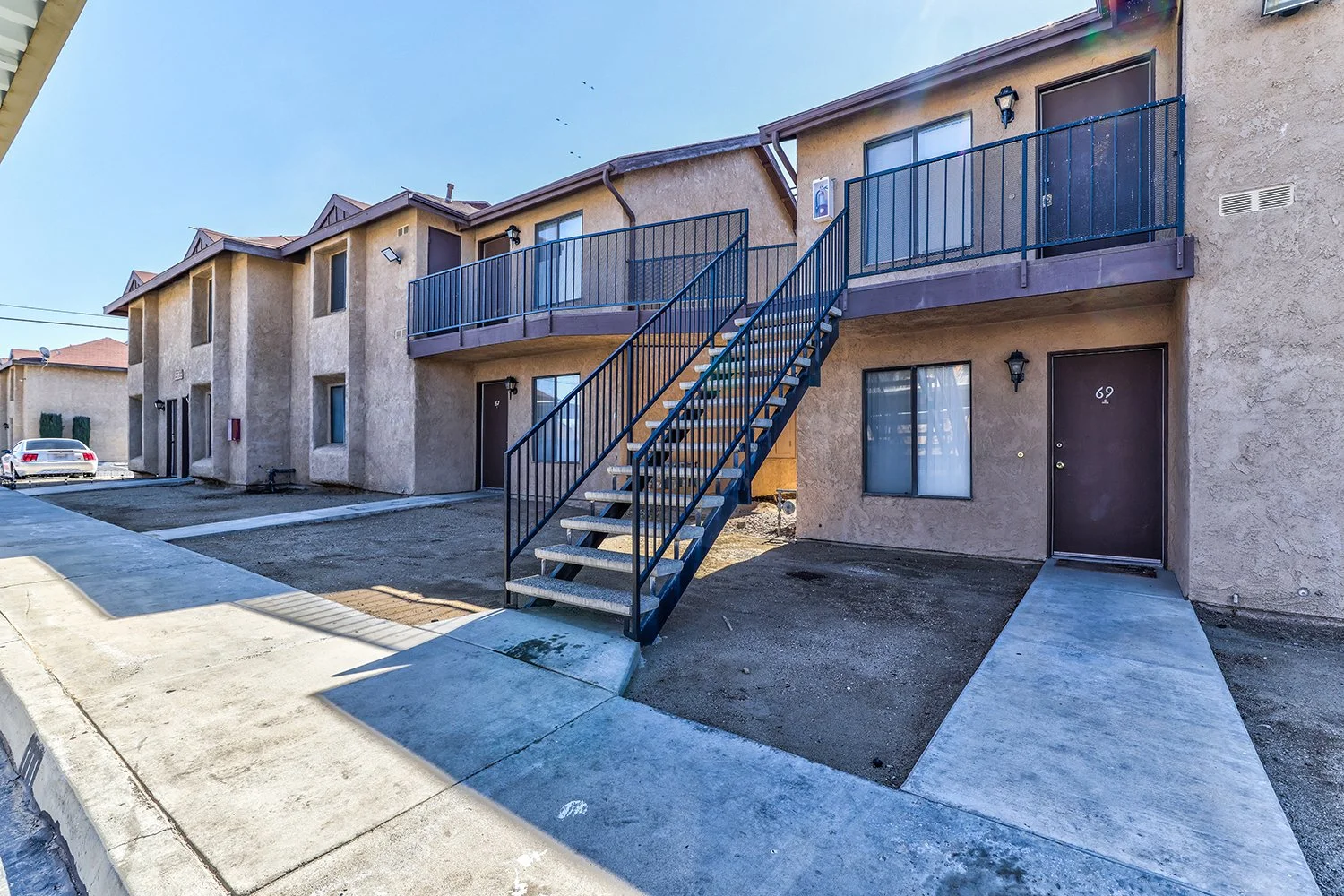 This image includes the exterior of the two-story apartment complex with large windows and a concrete path leading to each doorstep.