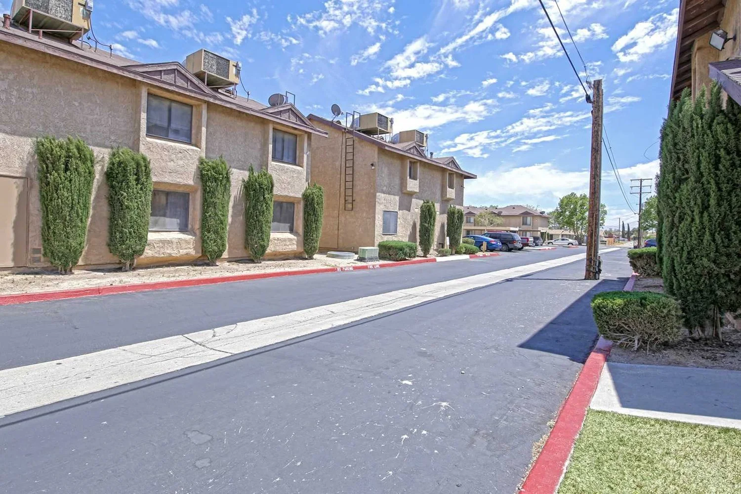 This image shows a long driveway lined by multi-story apartment buildings and neat green trees.