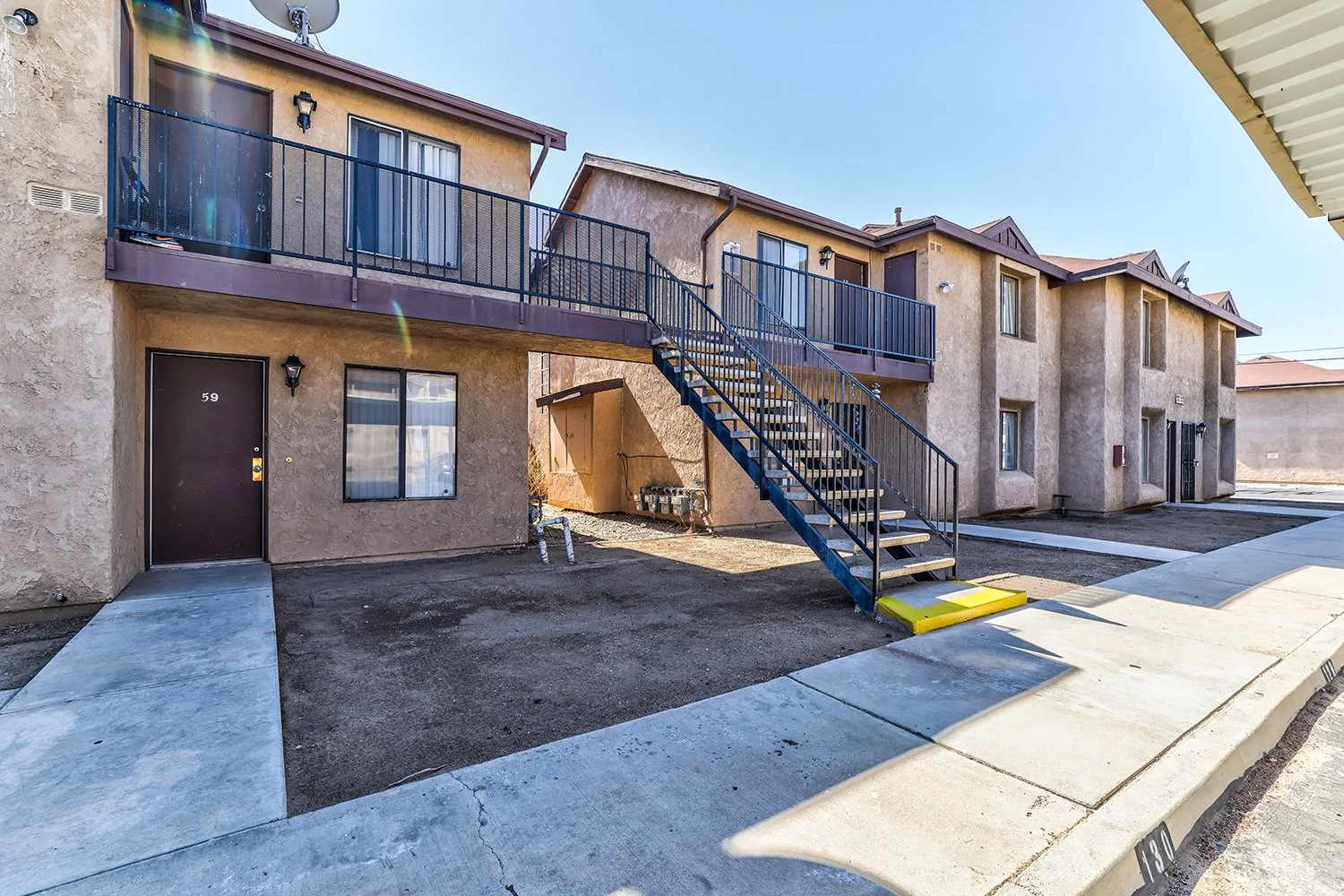 This image includes another angle of the exterior of the two-story apartment complex with large windows and a concrete path leading to each doorstep.