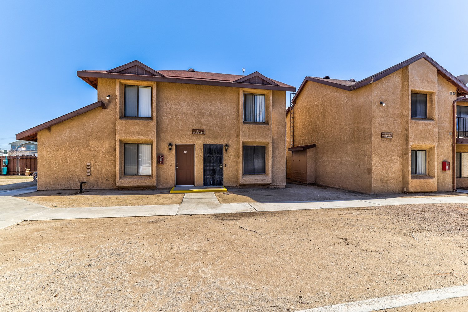 This image includes another angle of the exterior of the two-story apartment complex with large windows and a concrete path leading to each doorstep.