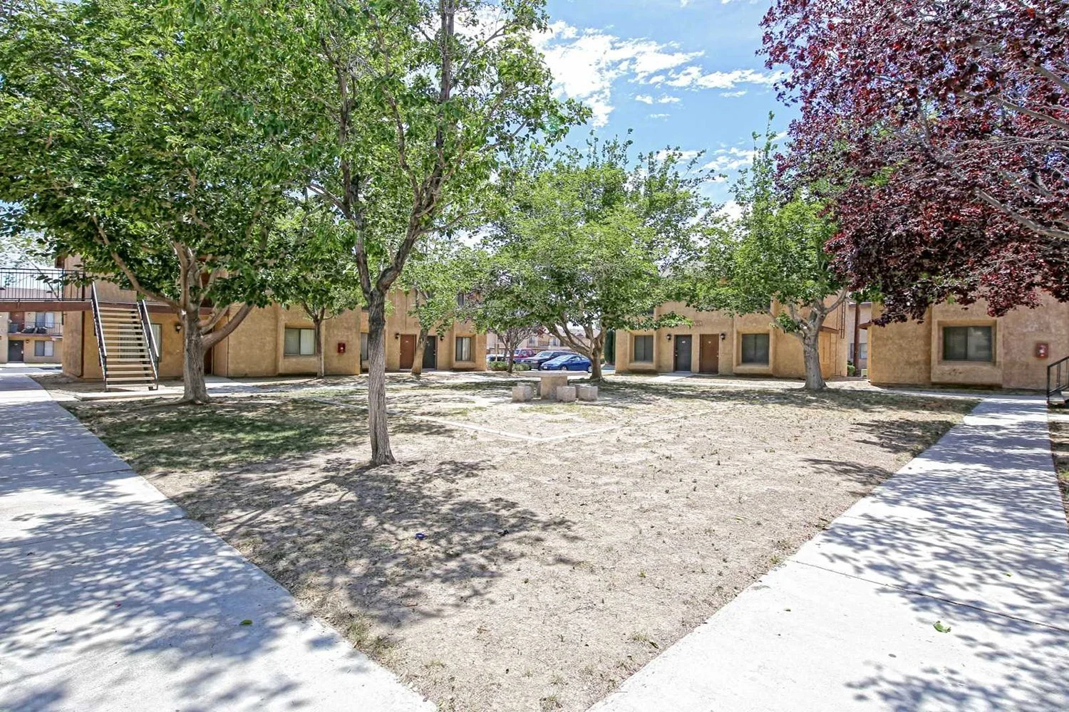 Another angle of the dirt courtyard with lush trees that includes a small seating area and a view of the building.
