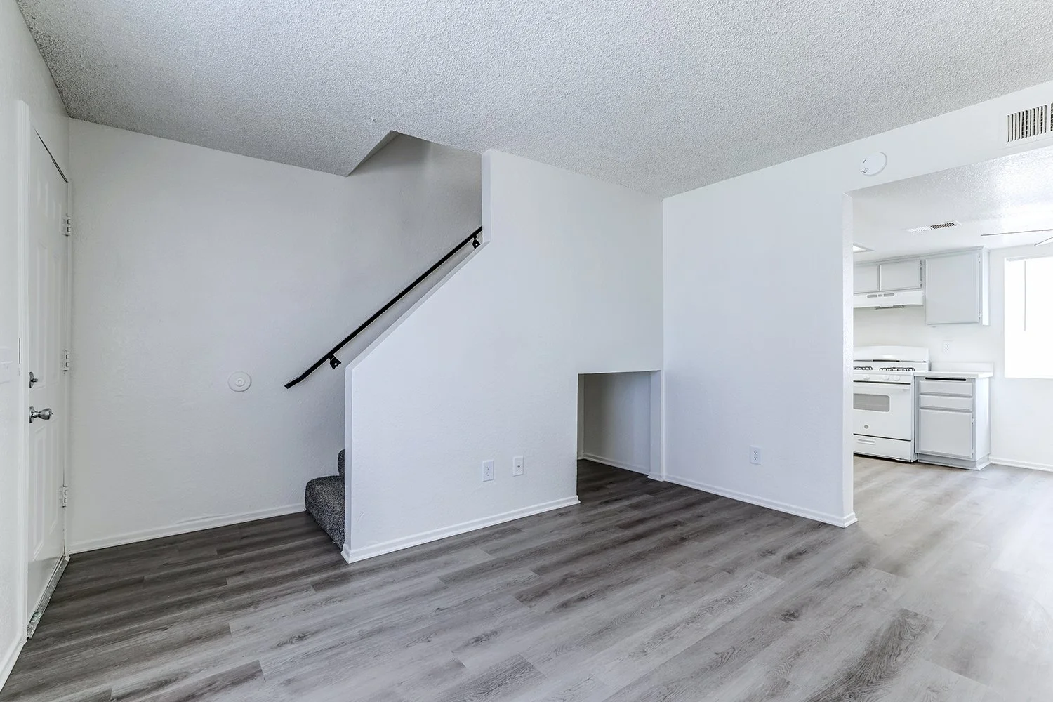 This image shows the interior of an empty apartment living room featuring gray wood-look flooring and plain white walls.