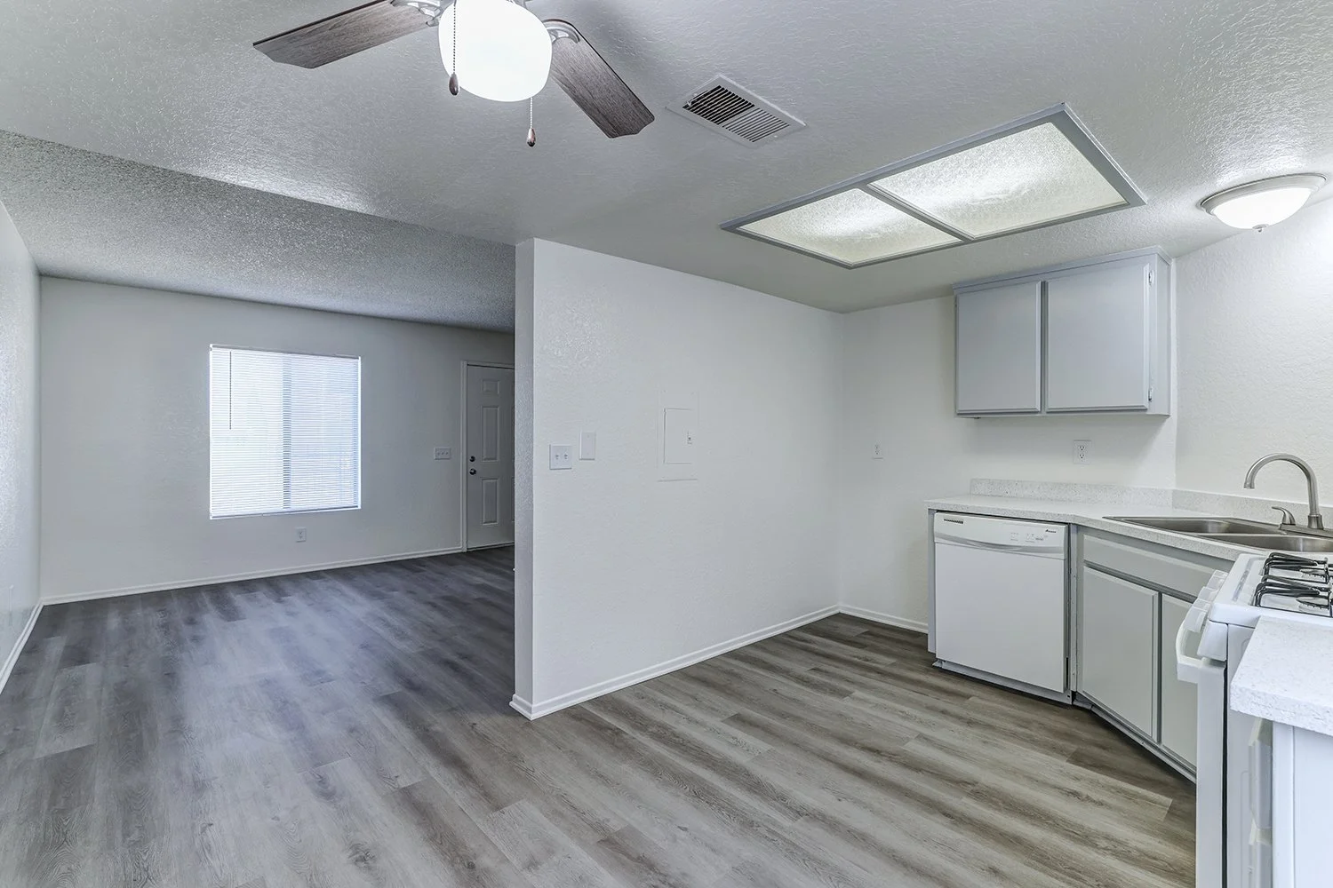 This image shows the interior of a kitchen featuring gray wood-look flooring and plain white walls.