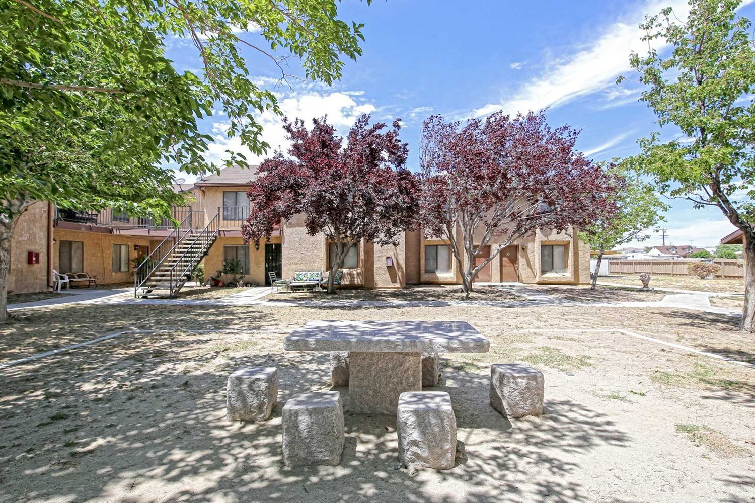 Another angle of the dirt courtyard with lush trees that includes a small seating area and a view of the building.