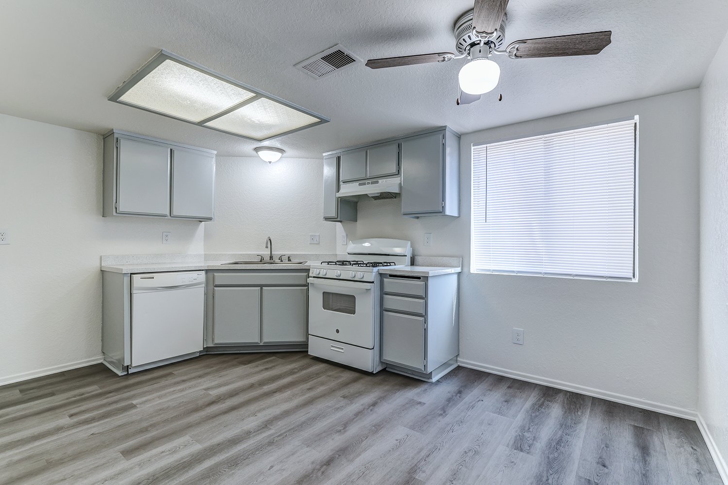 This image shows the interior of a kitchen featuring gray wood-look flooring and plain white walls.