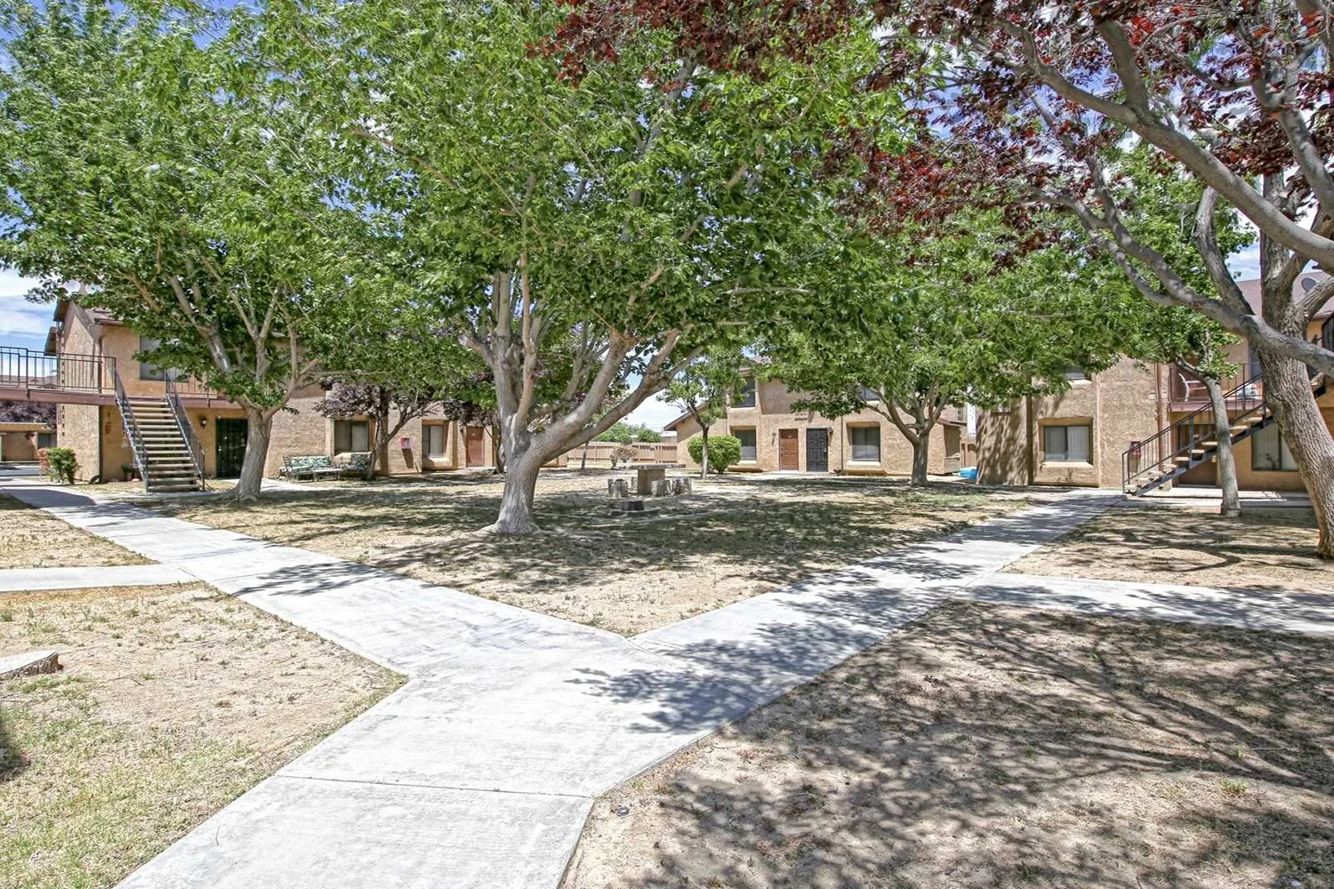 Another angle of the dirt courtyard with lush trees that includes a small seating area and a view of the building.