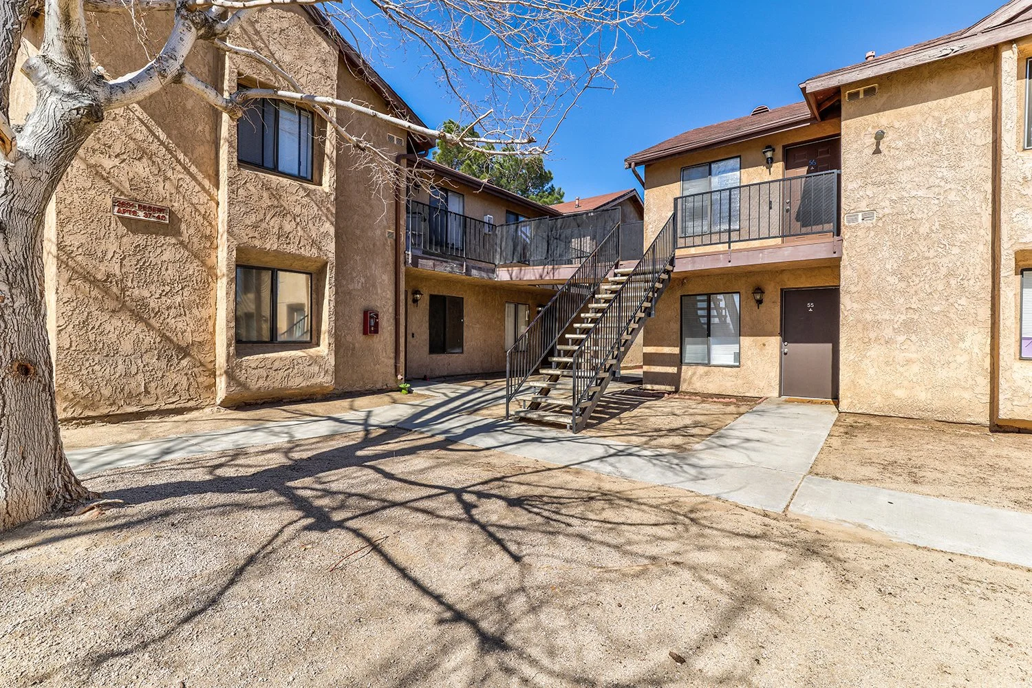 This image includes another angle of the exterior of the two-story apartment complex with large windows and a concrete path leading to each doorstep.