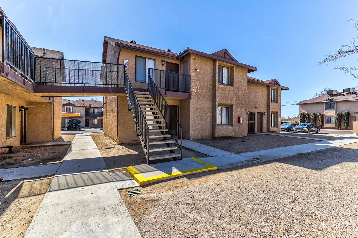 This image includes another angle of the exterior of the two-story apartment complex with large windows and a concrete path leading to each doorstep.