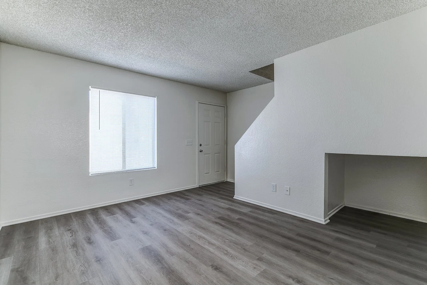 This image shows the interior of an empty apartment living room featuring gray wood-look flooring and plain white walls.