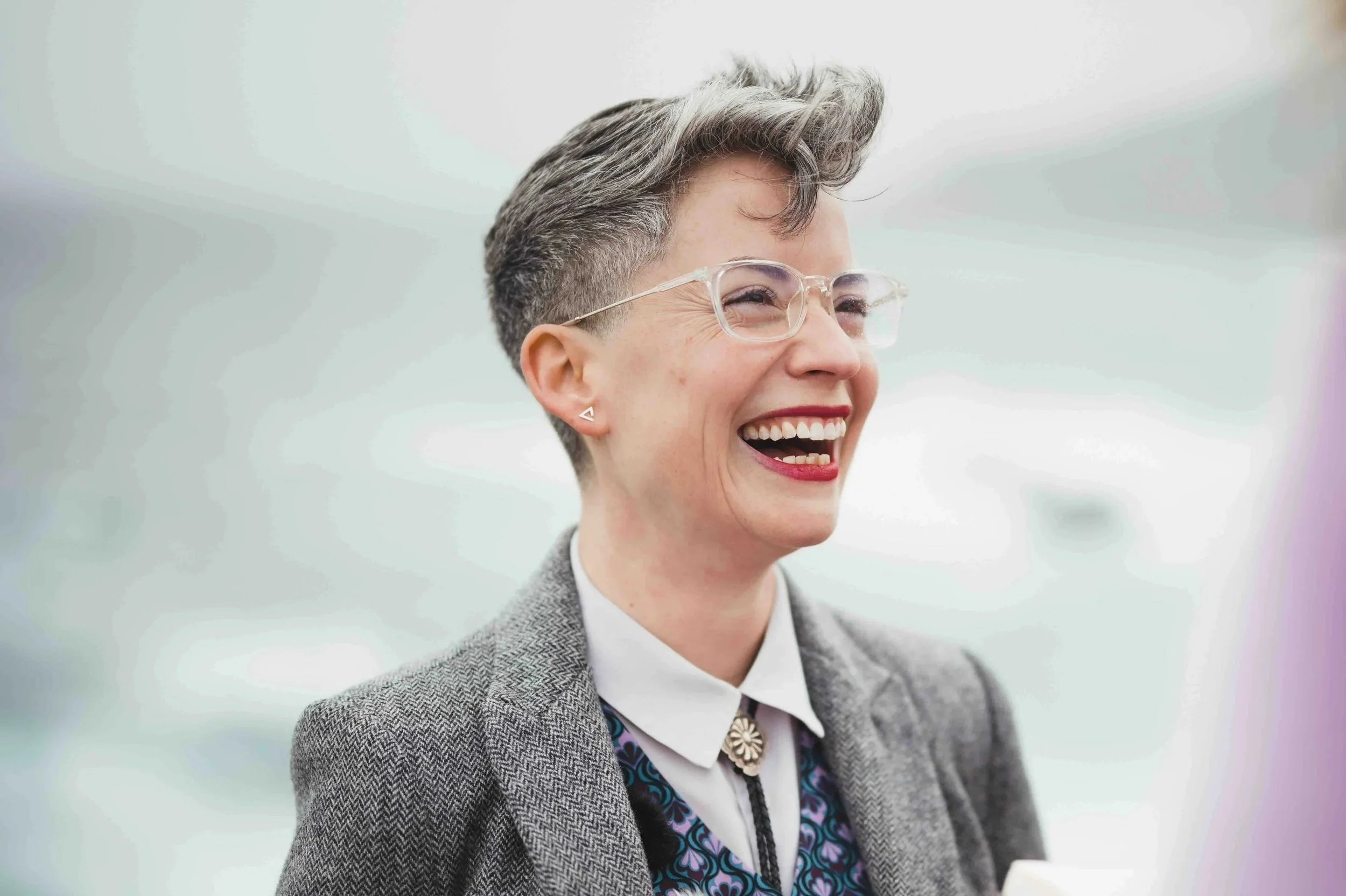 An androgynous person in a suit, laughing. Photo by Tatiana Scher Photography.