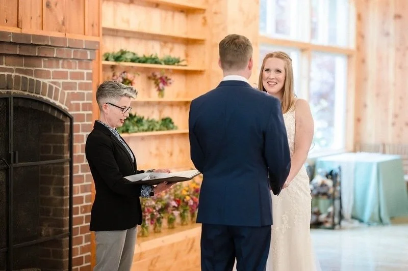 A couple standing hand-in-hand in front of a wedding officiant who is reading. Photo by Tatiana Scher Photography.
