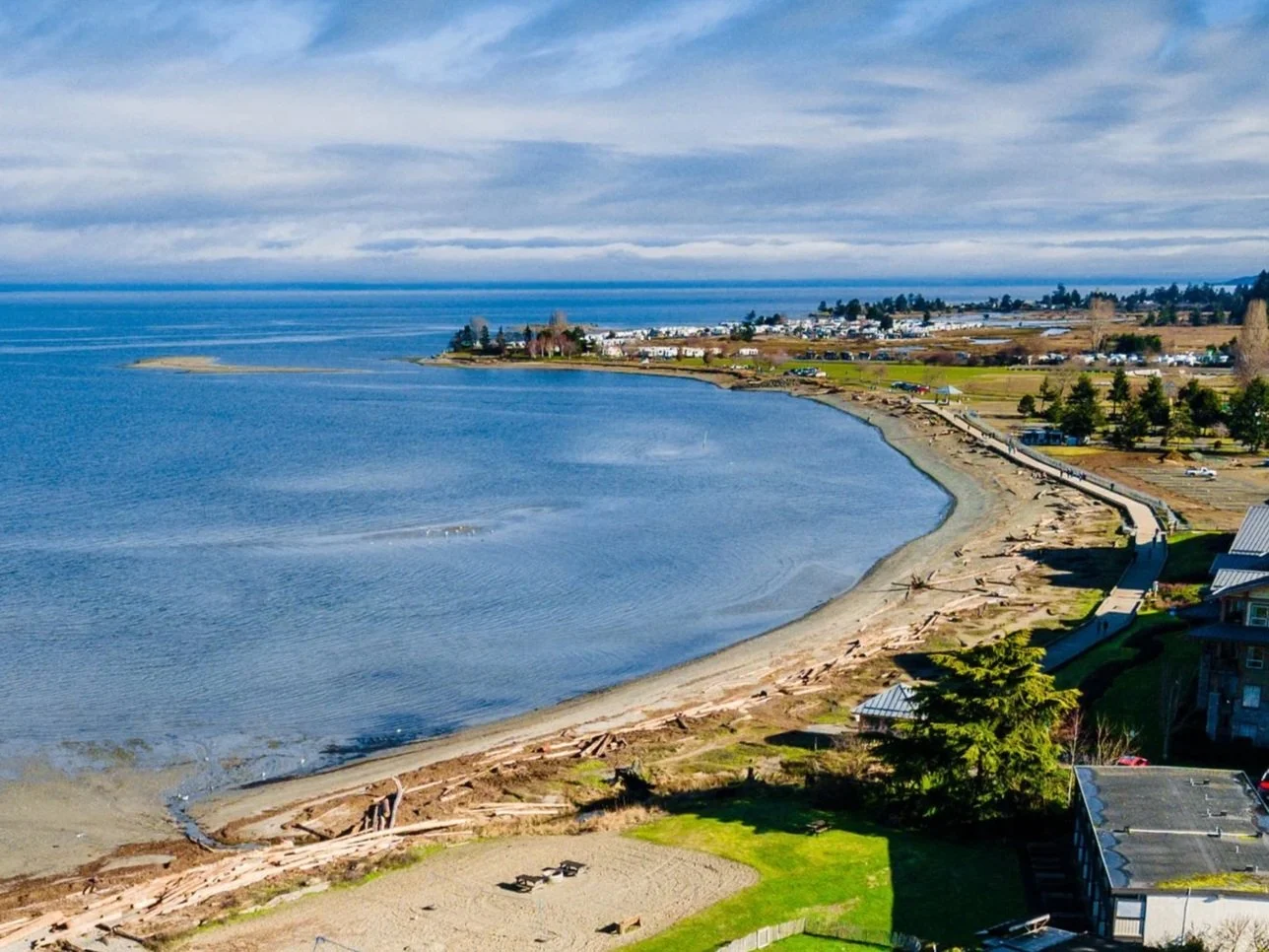 A coastal scene with a peninsula town, sandy beach, and calm blue water under partly cloudy skies.