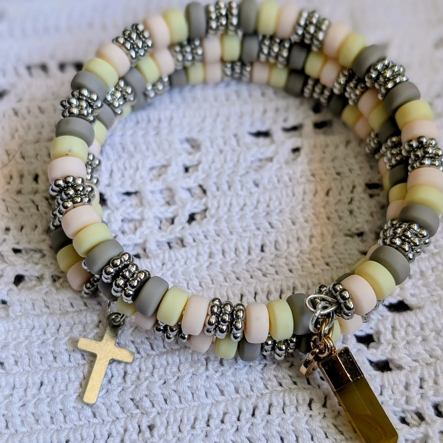 Our Wrap Bracelet is the perfect addition to any wardrobe! Using memory wire, this bracelet features two designs: natural wooden beads, a warm red/brown tone clay bead, a light gray clay bead, and two charms - one stone and one a heart with a cross; 