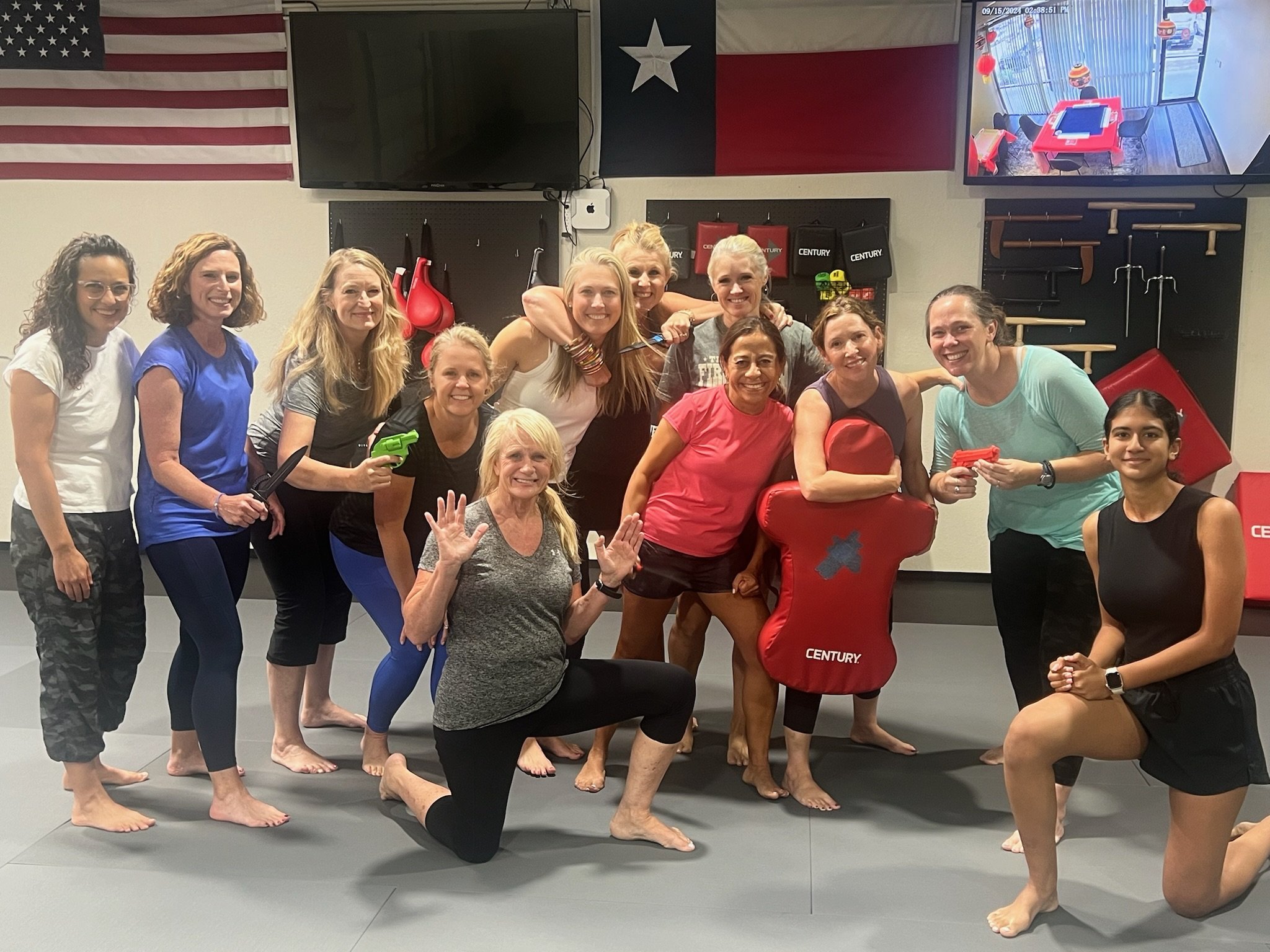 An older woman with short blonde hair and three young children in martial arts uniforms, holding certificates, smiling inside a martial arts studio.
